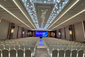 A conference room with rows of chairs, a large screen, and a modern ceiling design. - New Century Hotel (Tongxiang)