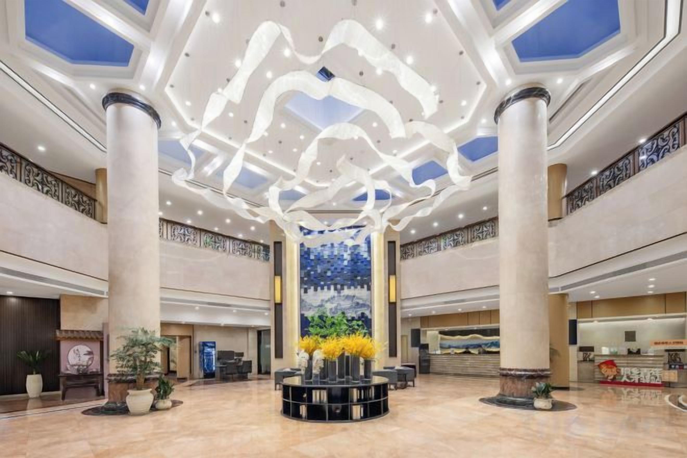 Un hall d’entrée spacieux, doté d’un plafond haut, de colonnes décoratives et d’un arrangement floral central.