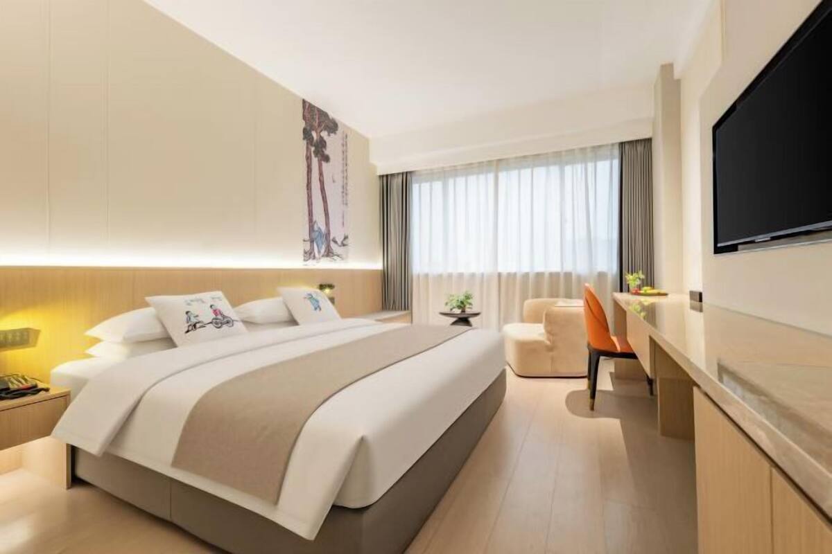 Quarto de hotel moderno com uma cama grande, uma escrivaninha, uma televisão e uma janela com cortinas.