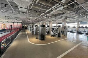 A gym with exercise equipment, a wooden floor, and a high ceiling with exposed pipes. - New Century Hotel (Tongxiang)