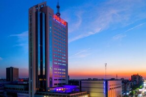 A high-rise hotel with multiple floors, a prominent antenna on top, and a lit sign indicating the hotel's name. - New Century Hotel (Tongxiang)