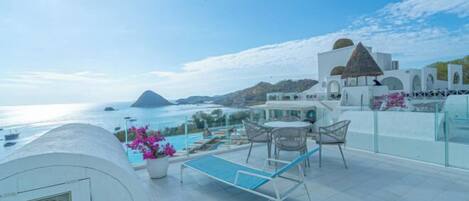 Una terraza en la azotea con piscina, sillas de descanso y vistas al mar.
