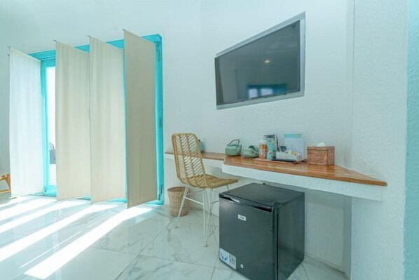 Une pièce comprenant un bureau, une chaise, un téléviseur fixé au mur et un petit réfrigérateur.