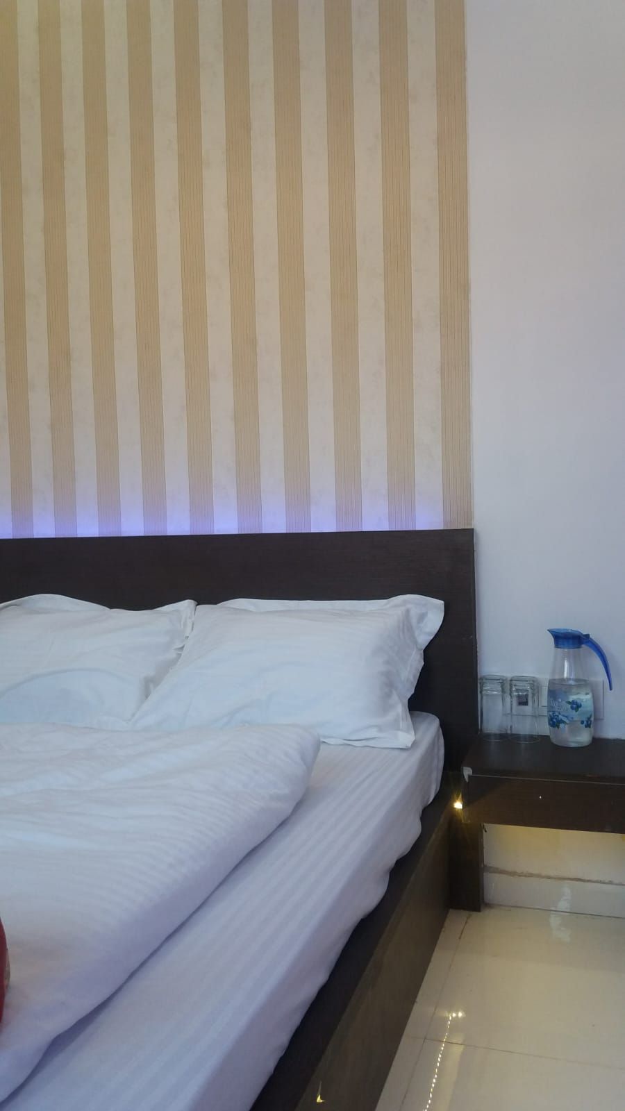 A neatly made bed with white linens, a dark headboard, and a striped wall behind it.