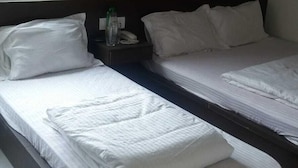 A hotel room with two single beds, a nightstand with a phone and a bottle, and a window with blinds. - Hotel Star City (Kolkata)