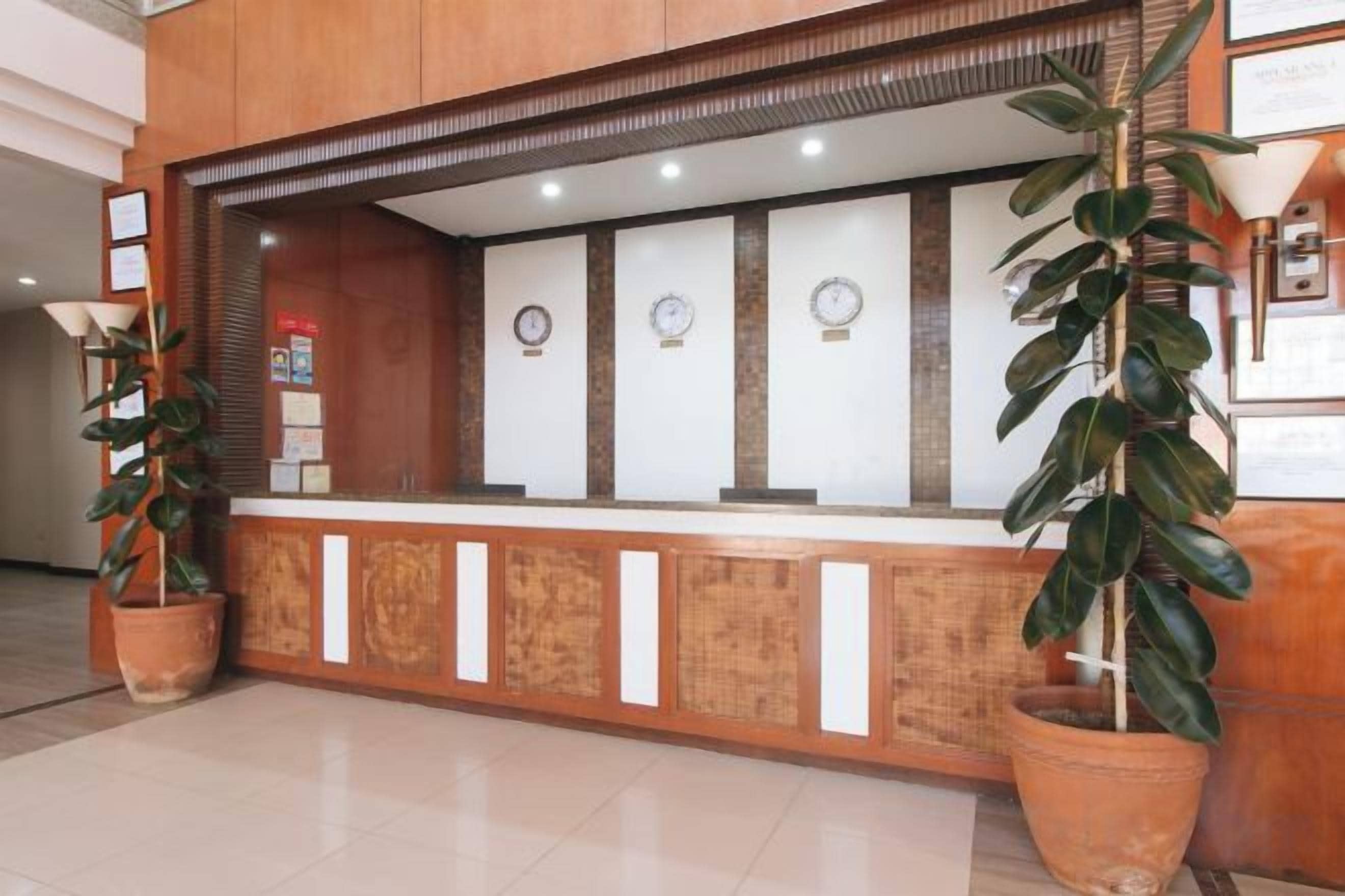 A reception desk with a wooden counter, potted plants, and wall clocks.