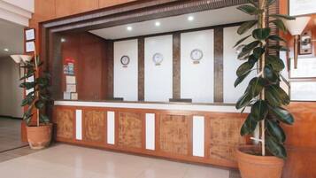 A reception desk with a wooden counter, potted plants, and wall clocks.