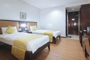 Una habitación de hotel con dos camas individuales, cabeceros de madera, ropa de cama blanca y suelo de madera.