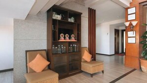 Eine Lobby mit einer Rezeption, zwei Korbstühle mit Kissen, einer Glastheke mit Auszeichnungen und einer Holzwand mit Zertifikaten.