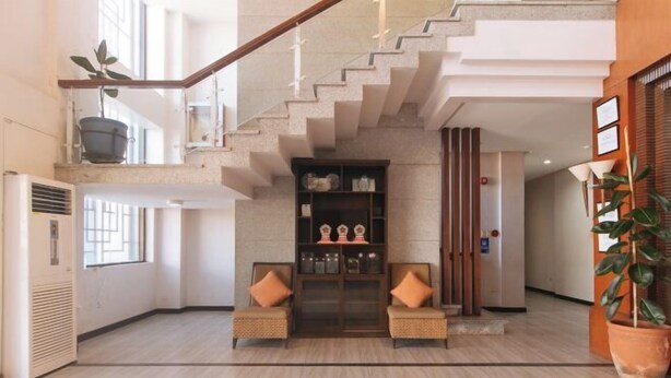 Eine geräumige Lobby mit einer Treppe, zwei gepolsterten Sessel, einem dekorativen Schrank und einer Zimmerpflanze.