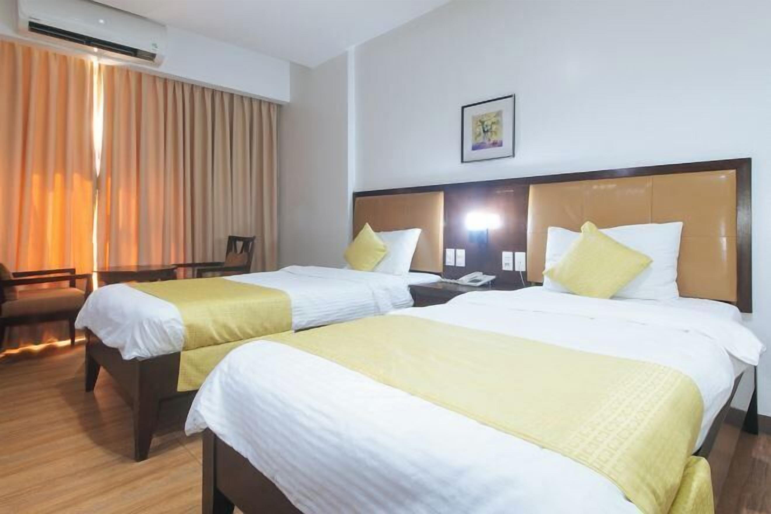 Habitación de hotel con dos camas, un escritorio, una silla y un ventanal grande con cortinas.