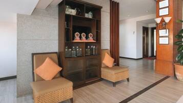A lobby with two wicker chairs, a wooden cabinet with decorative items, and a potted plant.