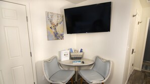 Ein kleiner Raum mit zwei Stühlen, einem Tisch, einem Flachbildfernseher und einem Bild an der Wand.