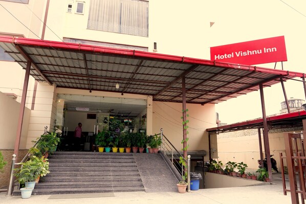 A hotel entrance with a red awning, a staircase, and potted plants. - Hotel Vishnu Inn (Dehradun)