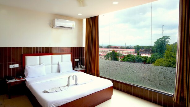 Ein Hotelzimmer mit einem großen Bett, einer Klimaanlage, einem Nachttisch, einem Telefon und Blick auf die Stadt durch ein großes Fenster.