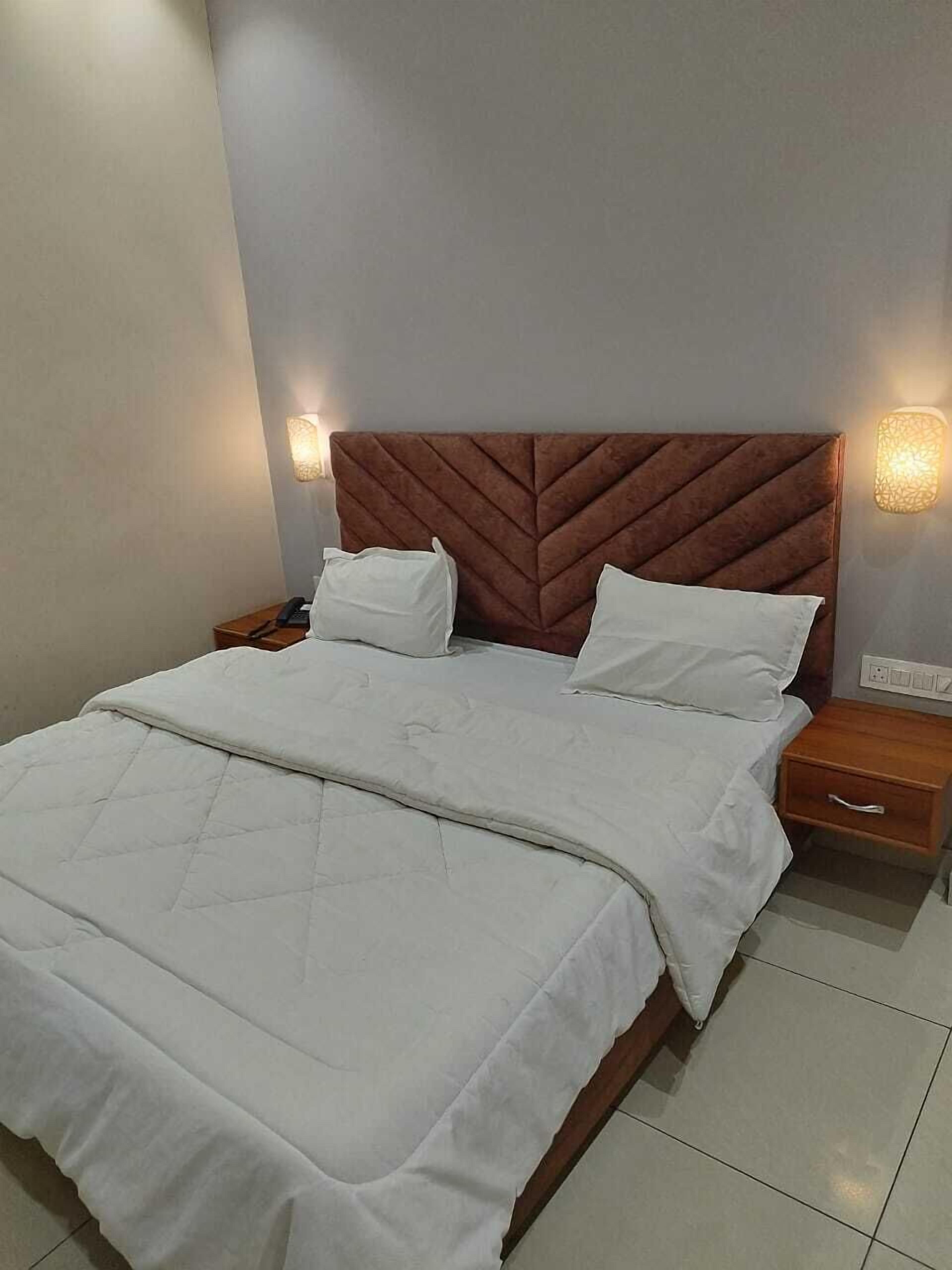 A neatly made bed with white linens, a wooden headboard, and two bedside tables with lamps.