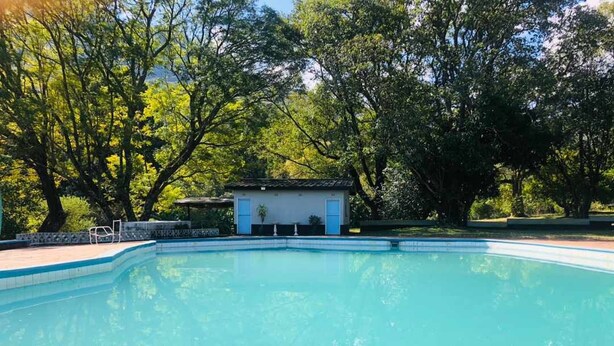 Una piscina con un pequeño edificio al fondo, rodeada de árboles.
