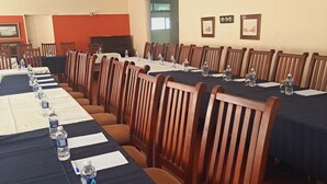 Un salón de conferencias con largas mesas, sillas, botellas de agua y documentos.