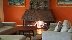 Una sala de estar con chimenea de piedra, dos cuadros con paisajes y un ventilador de techo.