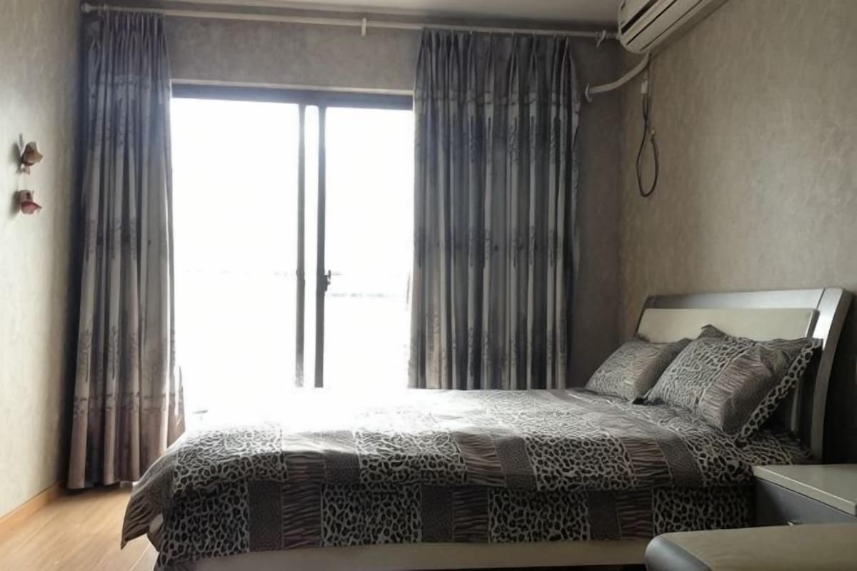 A bedroom with a bed, curtains, and a view through a window.