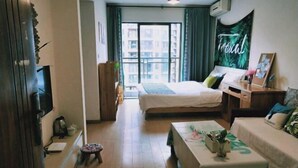 Une chambre à coucher comprenant un lit, un bureau, une chaise, un petit tabouret, une télévision et une fenêtre avec des rideaux.