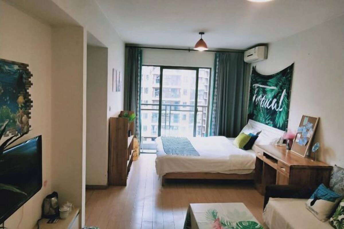 A bedroom with a bed, a desk, a TV, and a window with curtains.