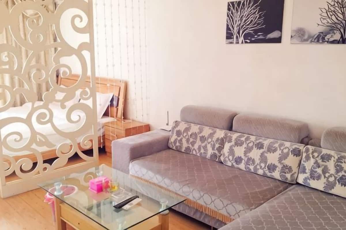 A living room with a sofa, a glass coffee table, a decorative partition, and a bed with a wooden headboard.