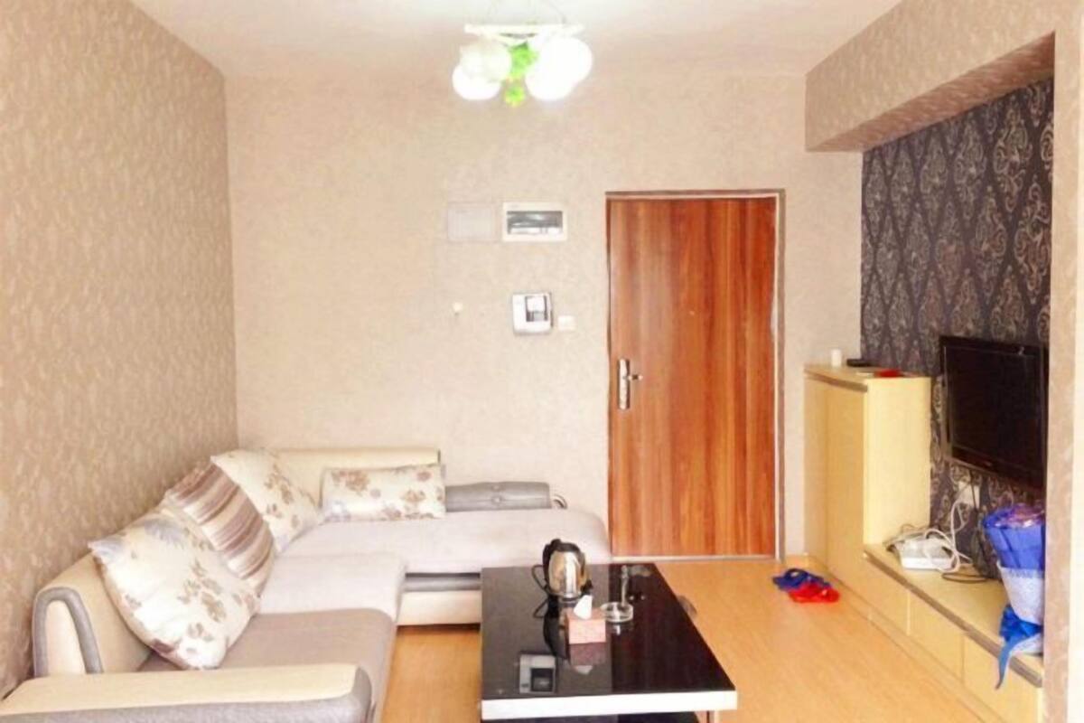 A living room with a sofa, a coffee table, a television, and a wooden door.