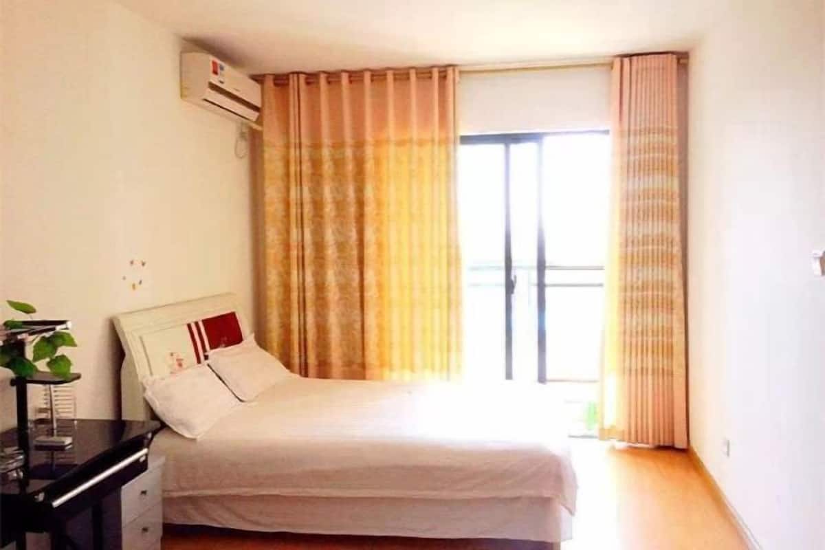 A bedroom with a bed, a desk, and a window with curtains.