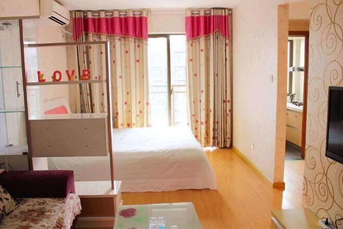 A bedroom with a bed, a bedside table, a mirror, and curtains.