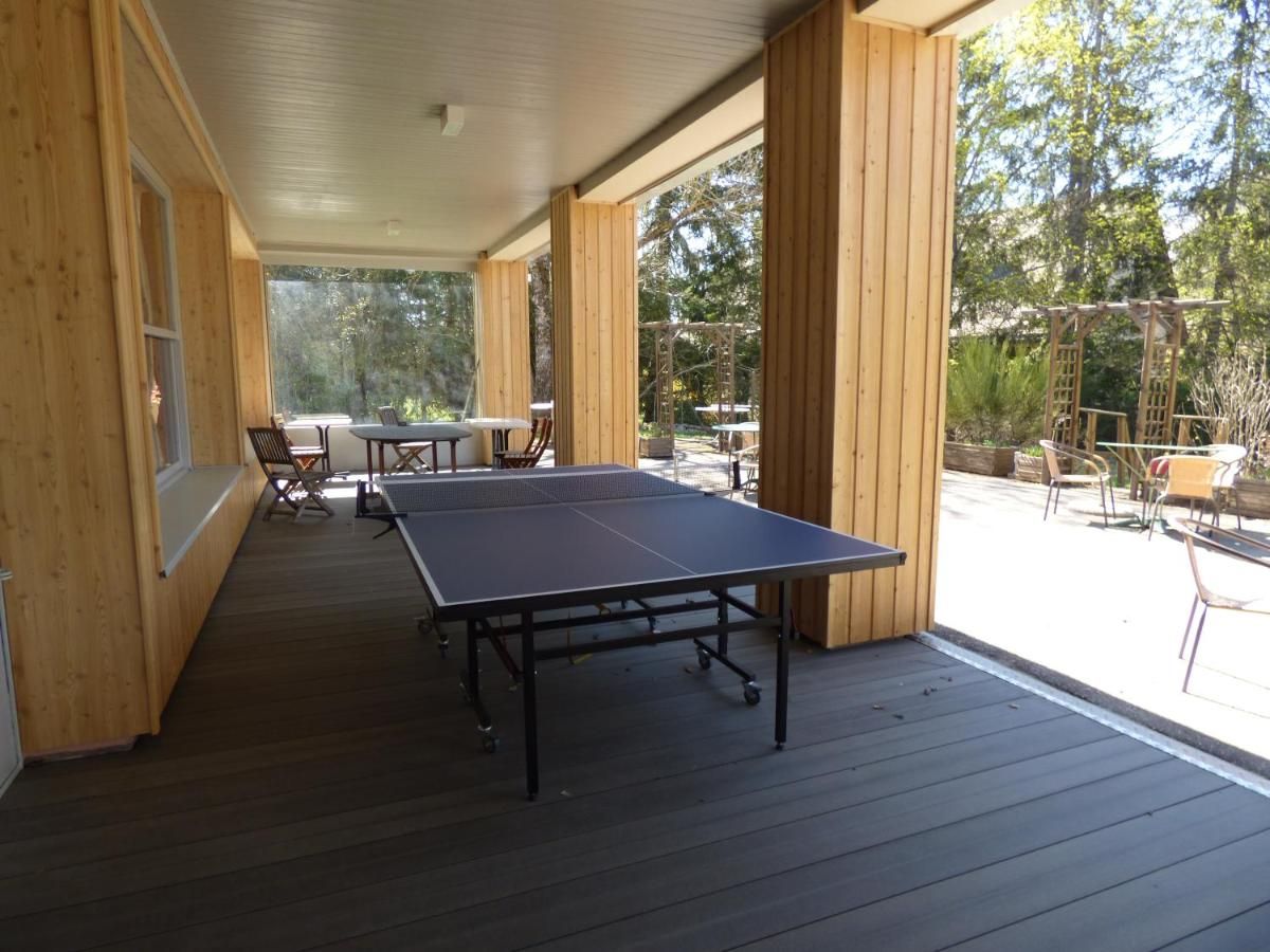 An outdoor wooden deck with a ping pong table and chairs, surrounded by wooden walls and large windows.