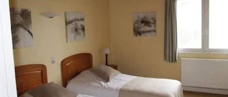 A room with two beds, a radiator, and artwork on the walls.
