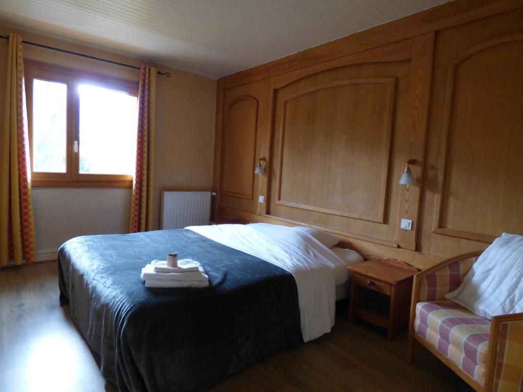 Quarto de hotel com uma cama grande, uma mesinha de cabeceira, uma cadeira e uma janela com cortinas.