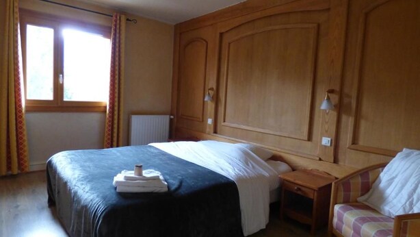 Habitación de hotel con una cama grande, una mesita de noche, una silla y una ventana con cortinas.