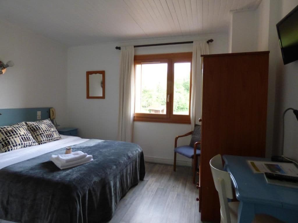 Un dormitorio con cama, escritorio, silla, ventana y televisor.