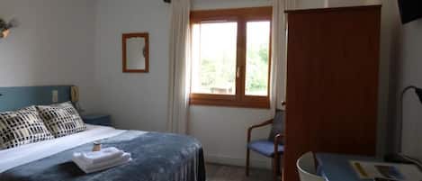 A bedroom with a bed, a desk, a chair, a window, and a TV.