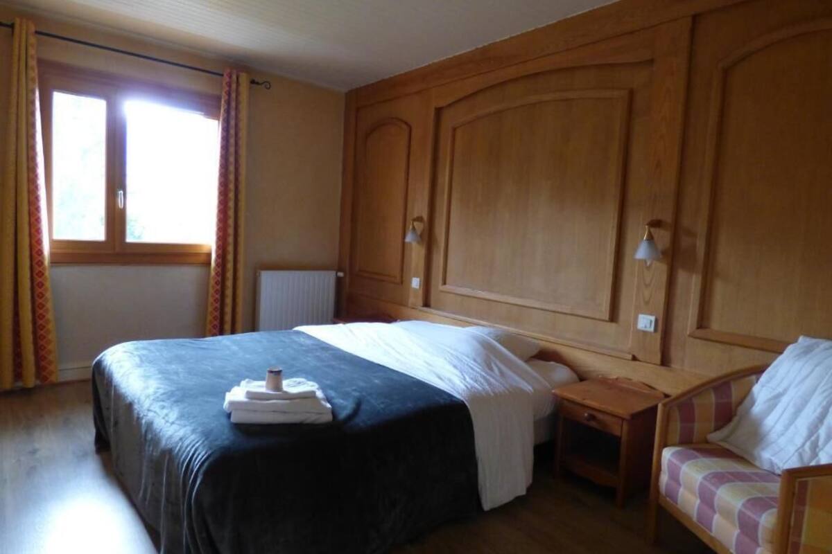 A hotel room with a large bed, a bedside table, a chair, and a window with curtains.