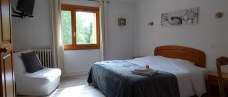 Une chambre à coucher avec un lit, une chaise, un radiateur, une fenêtre et un téléviseur.