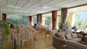 A spacious indoor area with multiple tables and chairs, large windows with curtains, and a mix of seating arrangements including sofas and chairs. - Logis Hotel La Cremaillere St Bonnet (Saint-Bonnet-en-Champsaur)