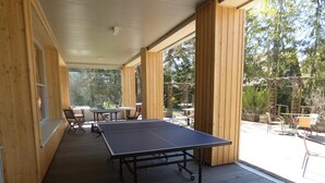 An outdoor wooden deck with a ping pong table and chairs, surrounded by wooden walls and large windows. - Logis Hotel La Cremaillere St Bonnet (Saint-Bonnet-en-Champsaur)