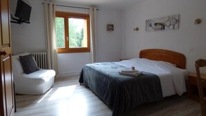 A bedroom with a bed, a chair, a radiator, a window, and a television. - Logis Hotel La Cremaillere St Bonnet (Saint-Bonnet-en-Champsaur)