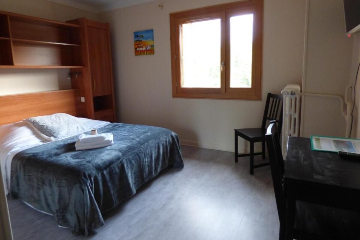 Un dormitorio con cama, escritorio, silla y ventana.