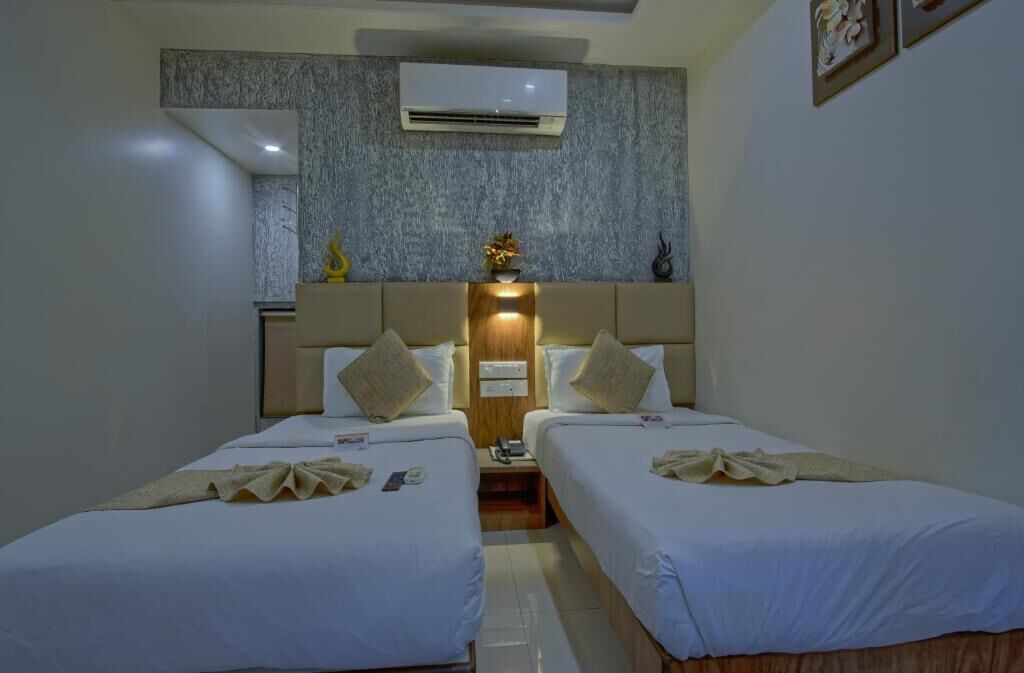 A hotel room with two single beds, a wooden headboard, an air conditioning unit, and a small table with a lamp.