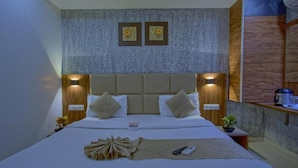 A modern hotel room with a large bed, two wall-mounted lamps, a wooden headboard, and a small bedside table with a plant. - Hotel Limra Surat (Surat)