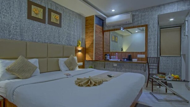 A hotel room with a large bed, a small desk, a mirror, and a chair. - Hotel Limra Surat (Surat)