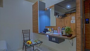 A hotel room with a wooden accent wall, a large mirror, a small table with fruits, a chair, and a potted plant. - Hotel Limra Surat (Surat)