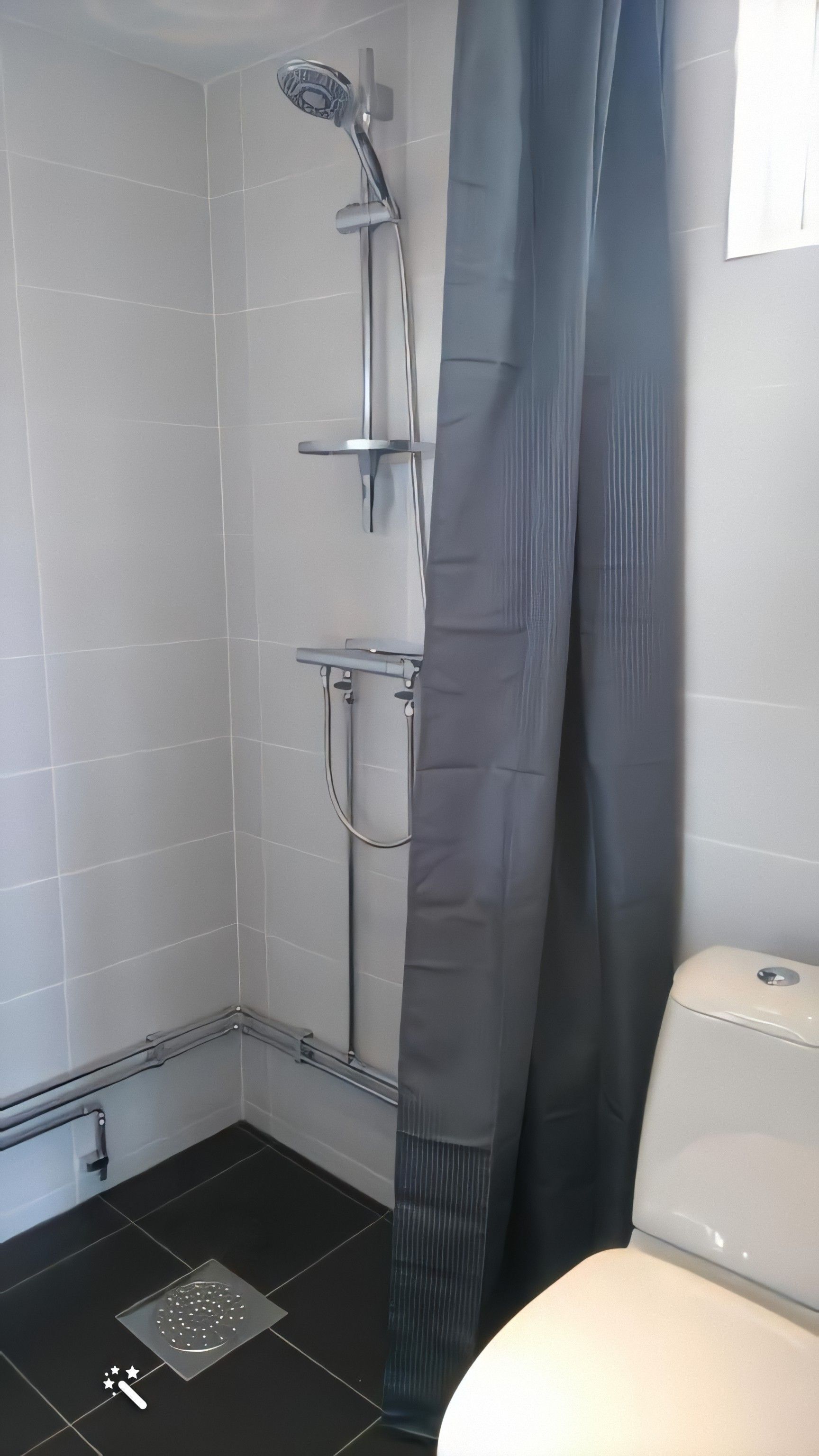 Ein Badezimmer mit Dusche, Toilette und Ablassdeckel auf dem Boden.