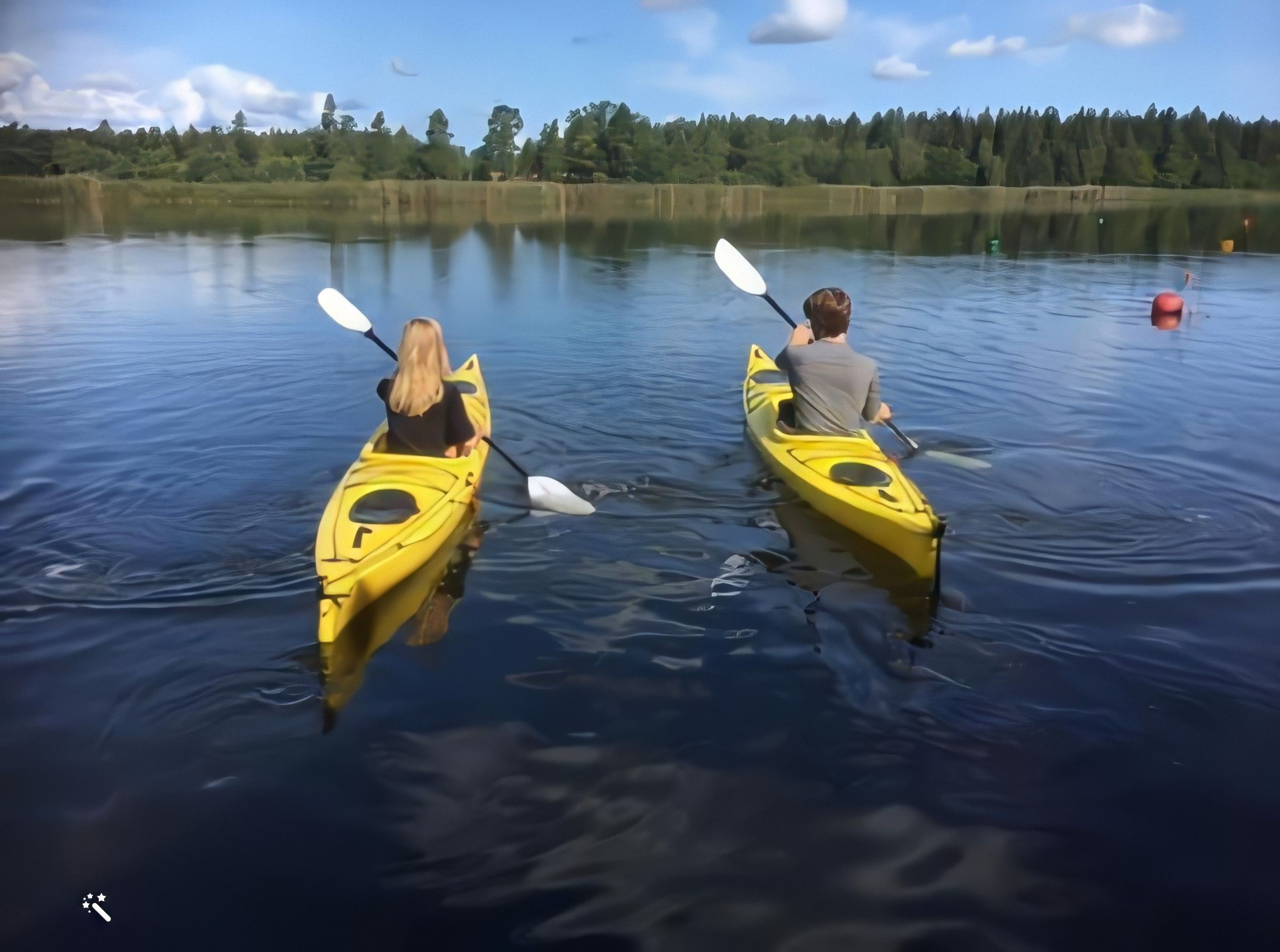 Two people kayaking on a calm lake with a forest in the background.