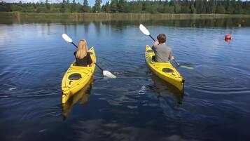 Two people kayaking on a calm lake with a forest in the background.
