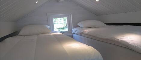 Un dormitorio con dos camas, una ventana y un techo inclinado con iluminación empotrada.